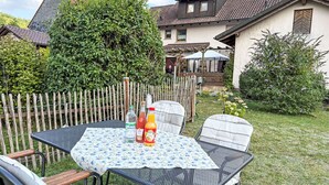 Eine Außenpatio mit Tisch und Stühlen, umgeben von einem Holzzaun und viel Grün.