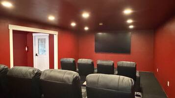A home theater room with red walls, a white door, and six black leather chairs.
