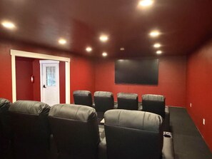A home theater room with red walls, a white door, and six black leather chairs.