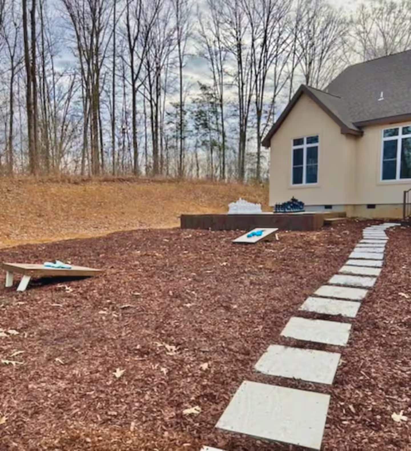 A residential area with a house, a paved path, and a wooded backdrop.