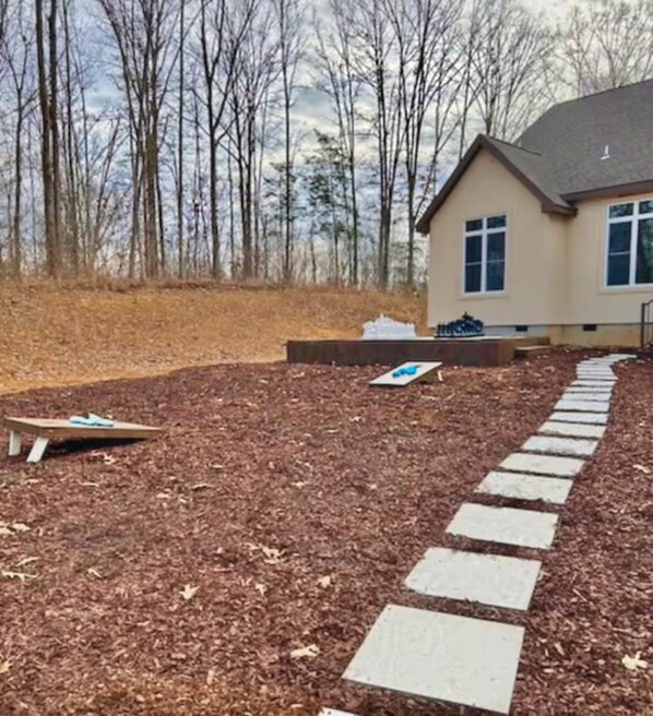 A residential area with a house, a paved path, and a wooded backdrop.
