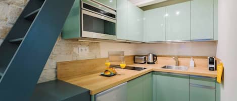 Una cocina moderna con armarios verdes, un refrigerador de acero inoxidable y una encimera de madera.