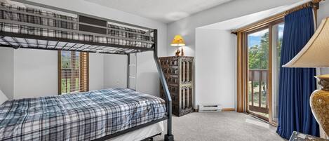 Una cama litera con colcha escocesa, un armario de madera con una lámpara y una ventana con cortinas.