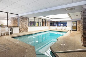 An indoor swimming pool with stone walls, a seating area with chairs, and a view of the adjacent room. - Silverado II Unit 631 Exquisite 4 bedroom penthouse, private deck, clubhouse (Winter Park)