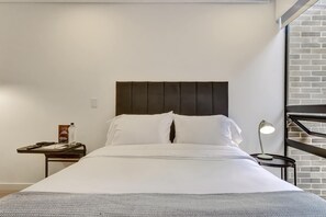 Ein Hotelzimmer mit Bett, Nachttisch, Lampe und einer Ziegelwand.
