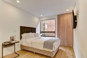 A bedroom with a bed, a bedside table, a TV mounted on the wall, and a window with a view of a brick building. - w Enchanting Cozy Loft in the Heart of Bogot (Bogotá)