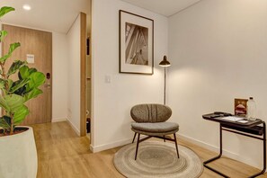 Ein modernes Zimmer mit Holzboden, einem Topfpflanzen, einem Sessel, einem runden Teppich, einem Schreibtisch mit Lampe und einem gerahmten Bild an der Wand.