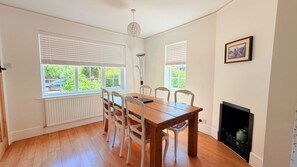 A dining room with a wooden table and white chairs, large windows with blinds, a floor lamp, and a fireplace. - Dutch Cottage Spacious 2-bed w Large Garden (Halstead)