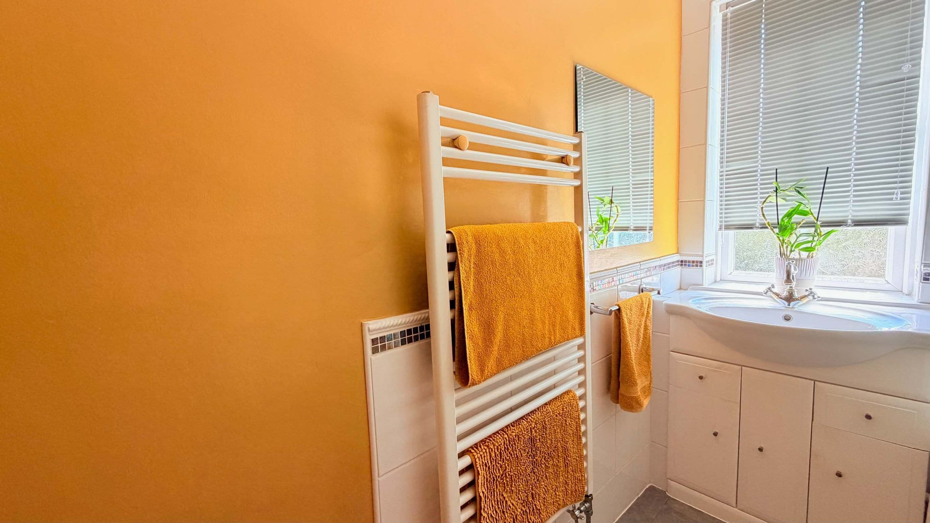 A bathroom with a white radiator, a sink with a mirror above it, and a window with blinds.