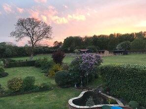 A well-maintained garden with a pond, surrounded by a wooden fence, and a large tree in the foreground. - Dutch Cottage Spacious 2-bed w Large Garden (Halstead)