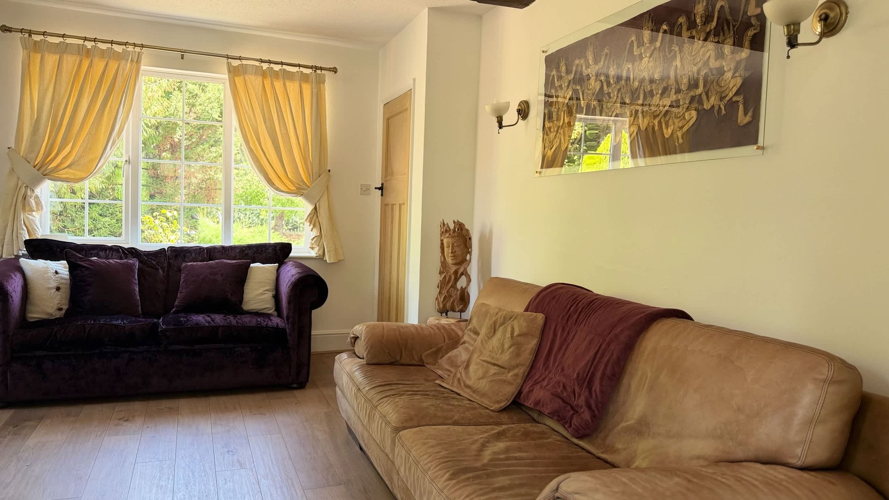 A living room with two sofas, a window with curtains, a wall-mounted light fixture, and a framed artwork.