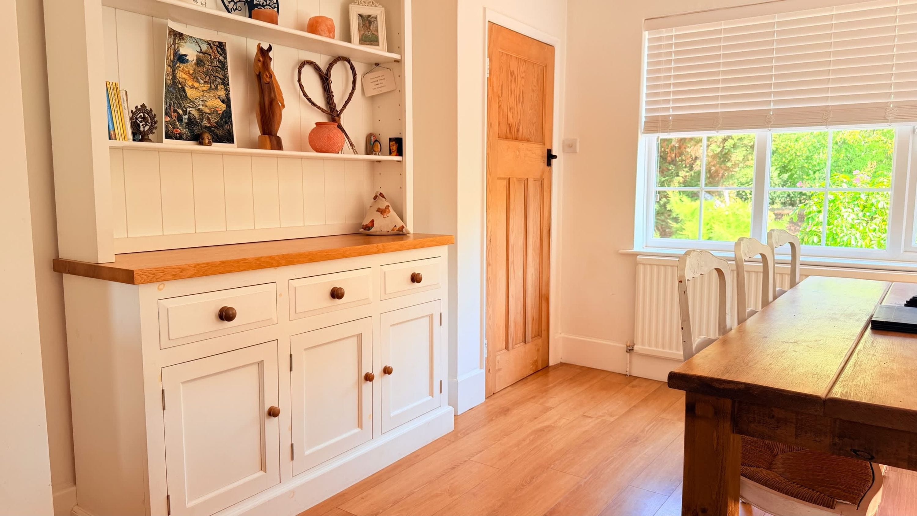 A kitchen with white cabinetry, a wooden countertop, and a window with blinds.