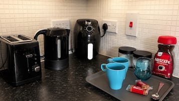 Un angolo cottura accessoriato con tostapane, bollitore, macchina del caffè e un vassoio con tazze e bustina di caffè.