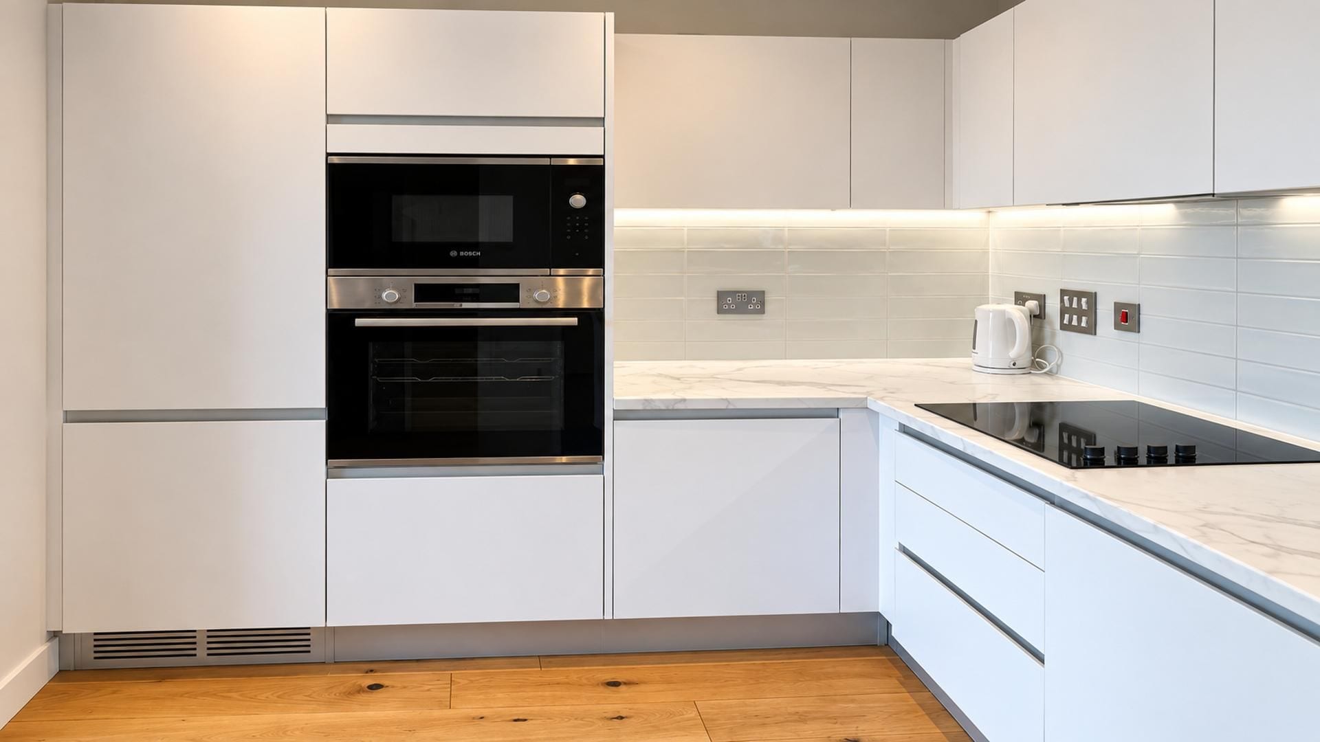 A modern kitchen with white cabinetry, a Bosch oven, a built-in stovetop, and a tiled backsplash.