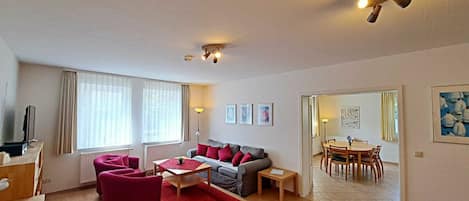 Een moderne woonkamer met een bank, fauteuils, een salontafel en een eethoek met een tafel en stoelen.