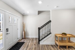Ein modernes Interieur mit einer Treppe, einer Tür mit Zahlenschloss, einer großen Vase und einem Korbtisch mit Pflanze.