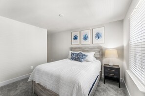 A bedroom with a bed, a nightstand, a lamp, and framed artwork on the wall. - Hide Tide at Lighthouse Bay (Ocean City)