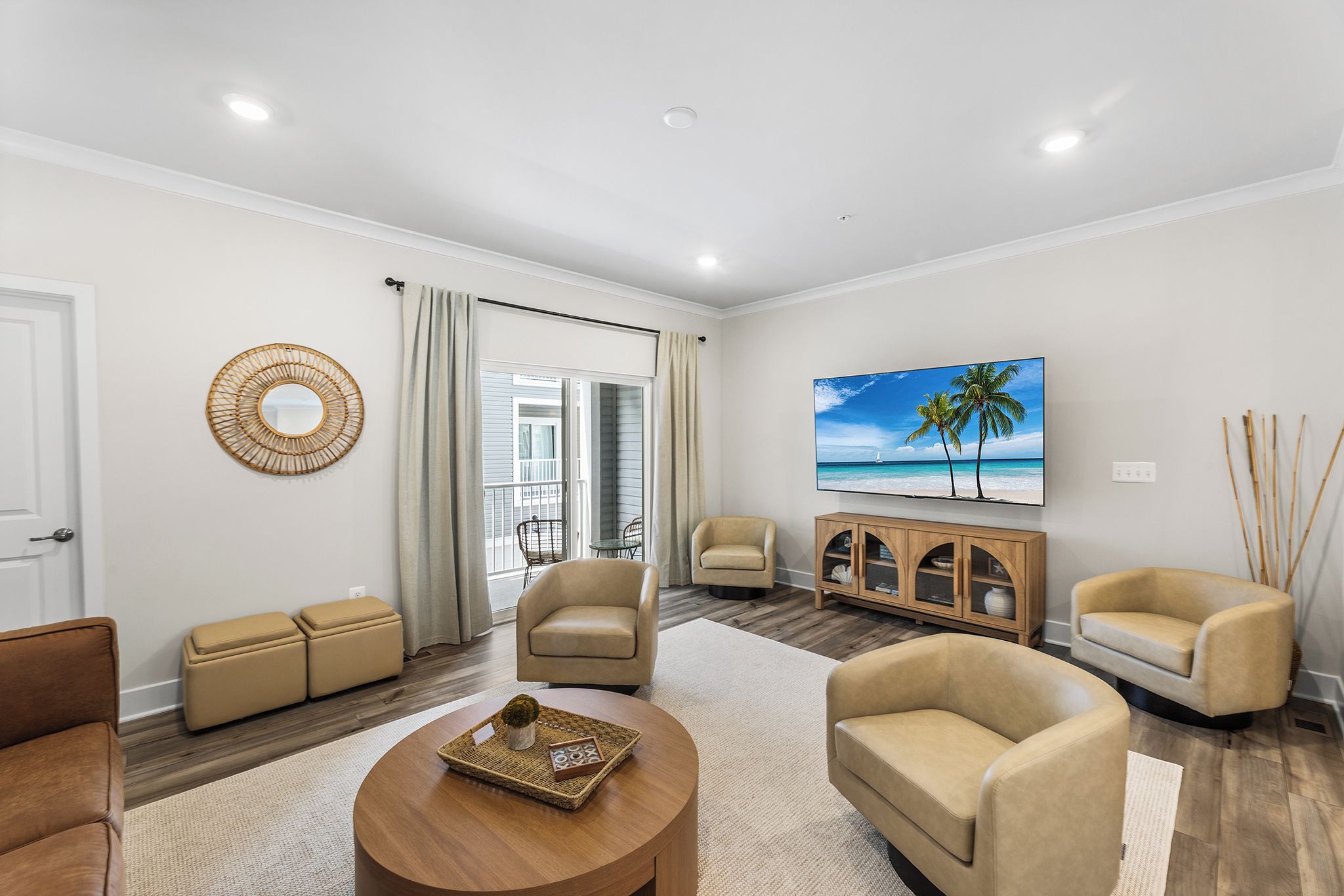 A modern living room with a sofa, armchairs, a coffee table, and a television displaying a beach scene.