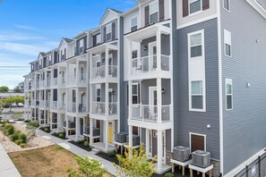 A row of multi-story apartment buildings with balconies, outdoor air conditioning units, and a clear sky. - Hide Tide at Lighthouse Bay (Ocean City)