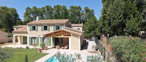 Una casa de dos pisos con piscina, mobiliario exterior y jardín.