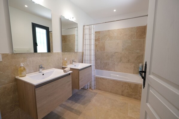 A modern bathroom with two sinks, a bathtub, and a shower.