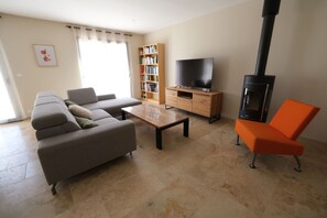 Ein Wohnzimmer mit einer Couch, einem Couchtisch, einem Fernseher auf einem Holzständer, einem Bücherregal und einem Kamin.