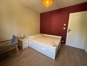 Ein Schlafzimmer mit einem Bett, einem Nachttisch, einer Lampe, einer Bank und einer Tür.