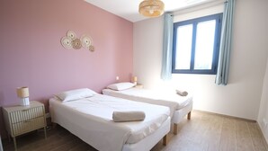 A bedroom with two beds, a nightstand, a lamp, and a window with curtains.