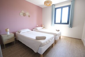 A bedroom with two beds, a nightstand, a lamp, and a window with curtains.