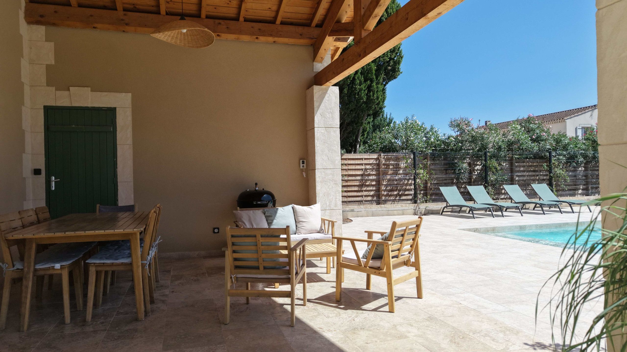 A covered outdoor area with a pool, wooden furniture, and a barbecue grill.