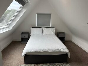 Un dormitorio con tragaluz, una cama con ropa de cama blanca, dos mesitas de noche y un cabecero.