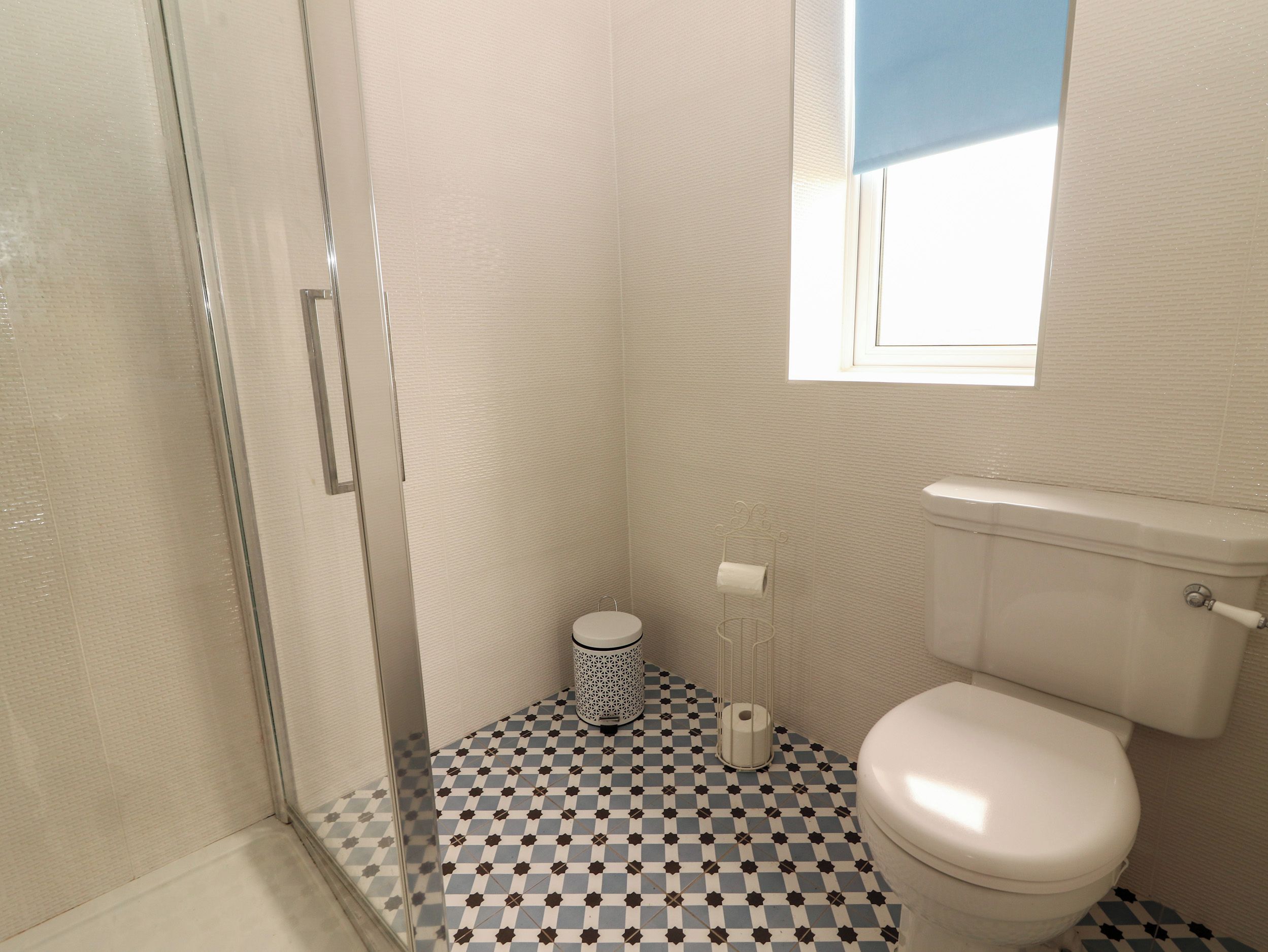 Une salle de bain avec un carrelage à motifs géométriques, des toilettes, une douche et une fenêtre.