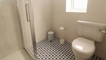 Une salle de bain avec un carrelage à motifs géométriques, des toilettes, une douche et une fenêtre.