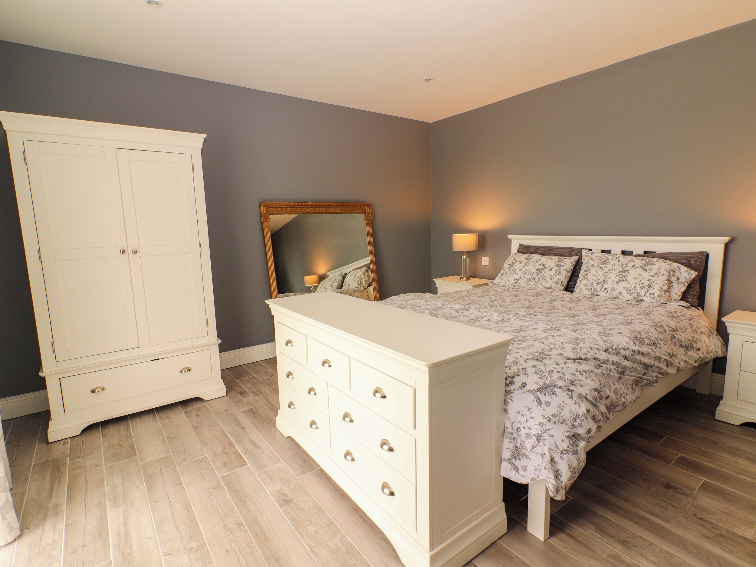 Ein Schlafzimmer mit Bett, Kommode, Kleiderschrank und Spiegel.