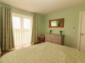 A bedroom with a bed, a dresser, a mirror, and a window with curtains. - CEOL NA MARA, family friendly, with a garden in Doonbeg, County Clare (Doonbeg)