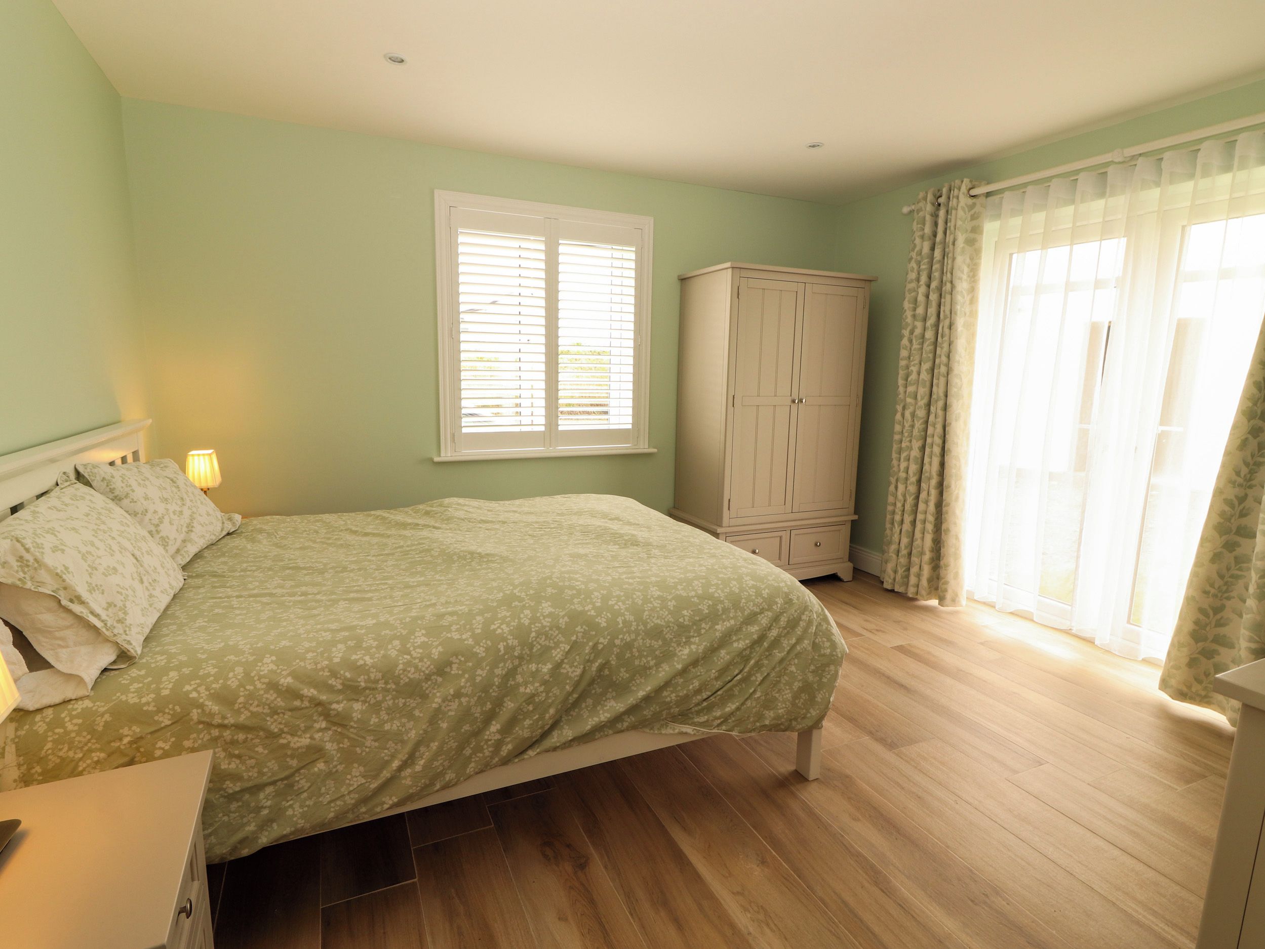 A bedroom with a bed, a wardrobe, a window with blinds, and a curtain.