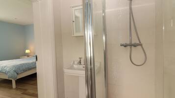 A bathroom with a shower, sink, and a bed in the adjacent room.