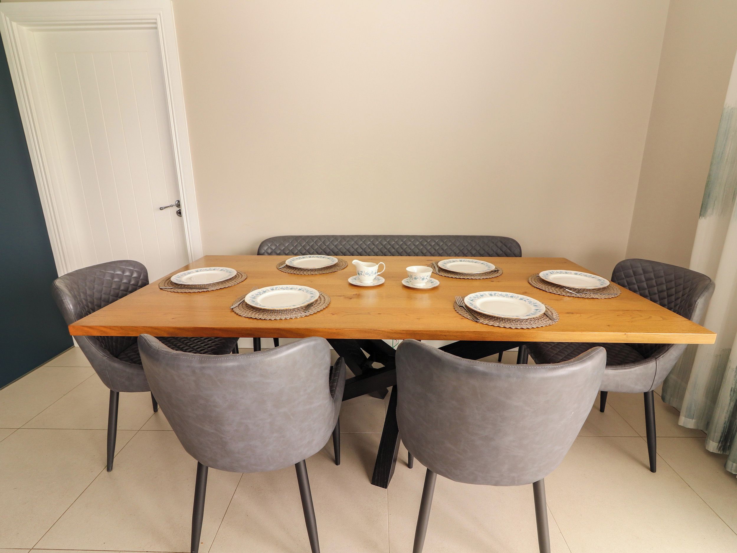 A dining table with six chairs, plates, and a pitcher.