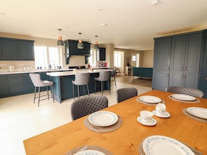 A modern kitchen with dark blue cabinets, a central island with bar stools, and a dining area with a wooden table set for four.
