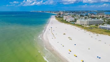 A beach with a long stretch of sand, a few umbrellas, and buildings in the background.