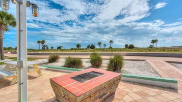 A paved outdoor area with a brick planter, picnic tables, and a clear view of a road and palm trees in the distance.