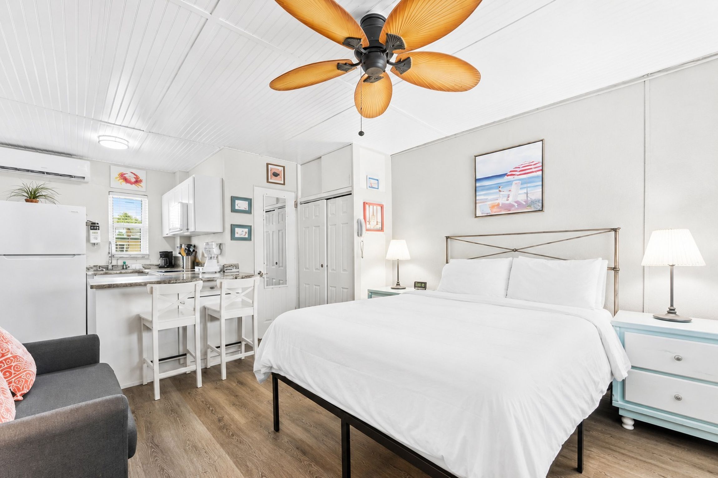 Habitación de hotel con cama, escritorio, silla, mesita de noche, lámpara y ventilador de techo.