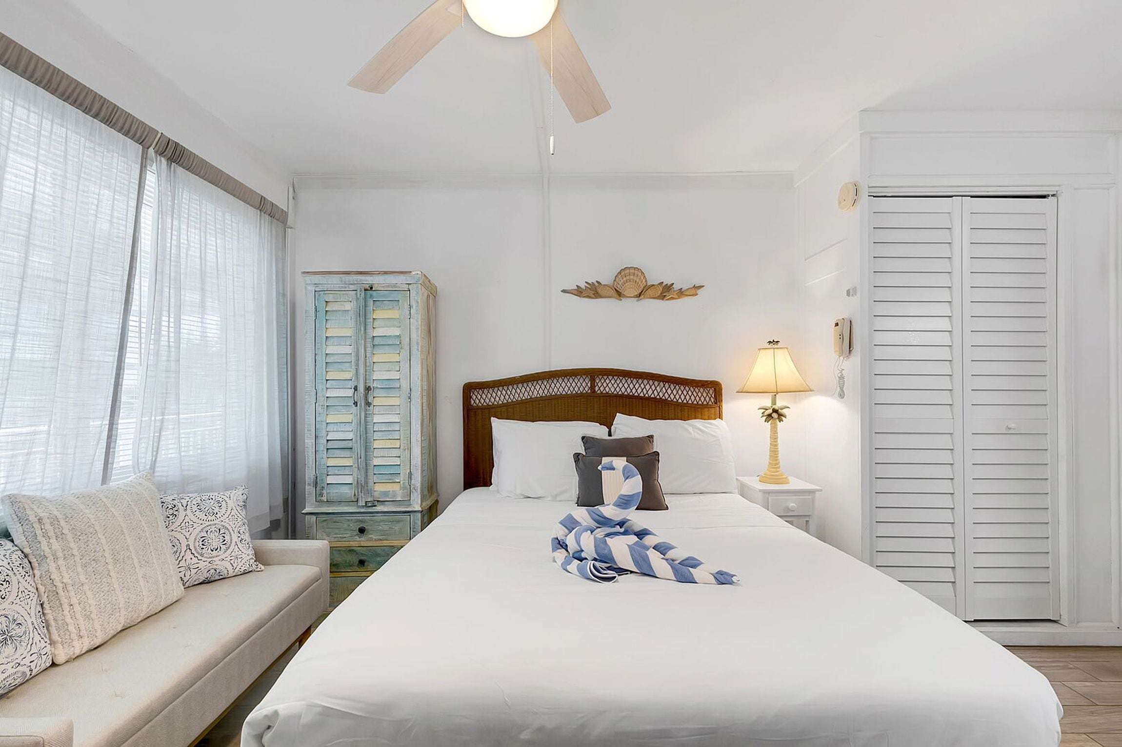 A hotel room with a bed, a nightstand, a lamp, a wardrobe, and a window with curtains.