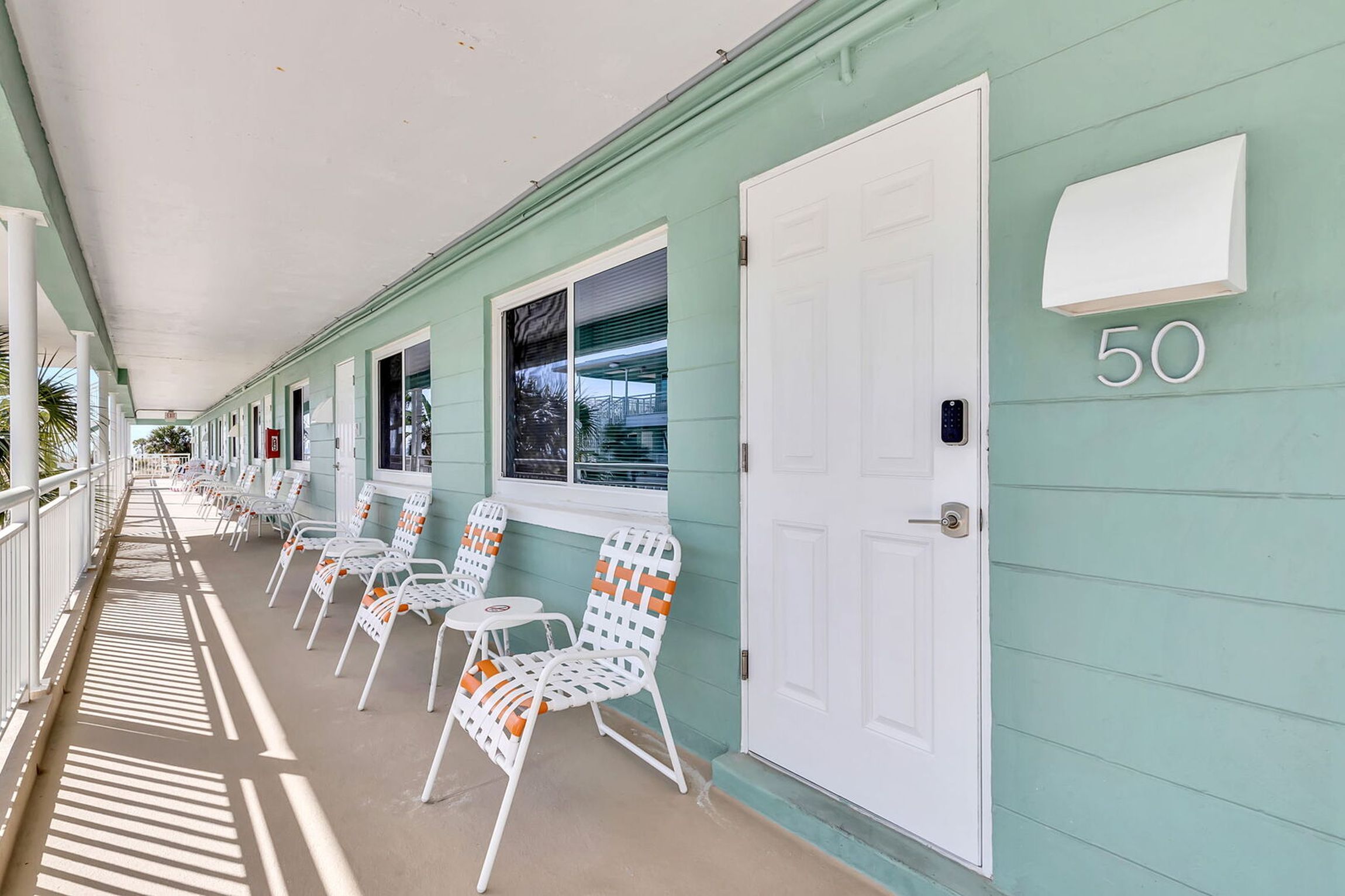 A corridor with white chairs and tables, a covered walkway, and a building number '50' on the wall.