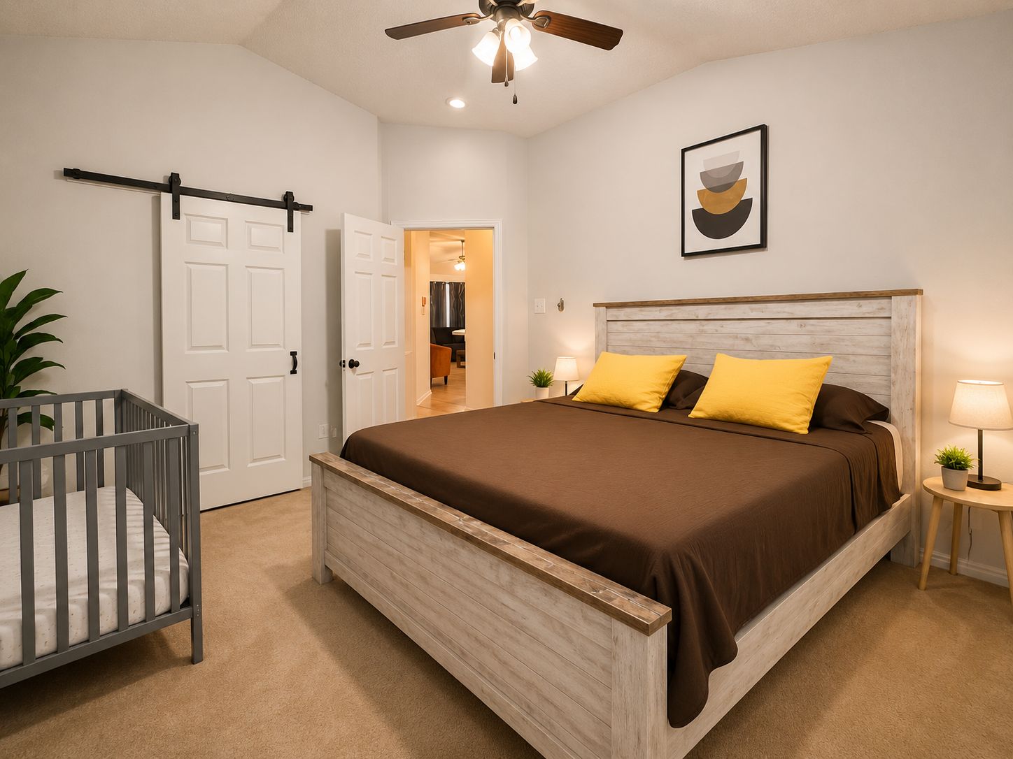 A bedroom with a wooden bed, a crib, a ceiling fan, and a door leading to another room.