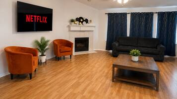 A living room with a fireplace, a sofa, two armchairs, a coffee table, and a TV mounted on the wall.