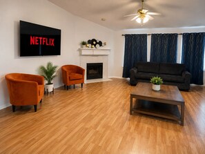 Ein Wohnzimmer mit Kamin, einer Couch, zwei Sesseln, einem Couchtisch und einem an der Wand montierten Fernseher.