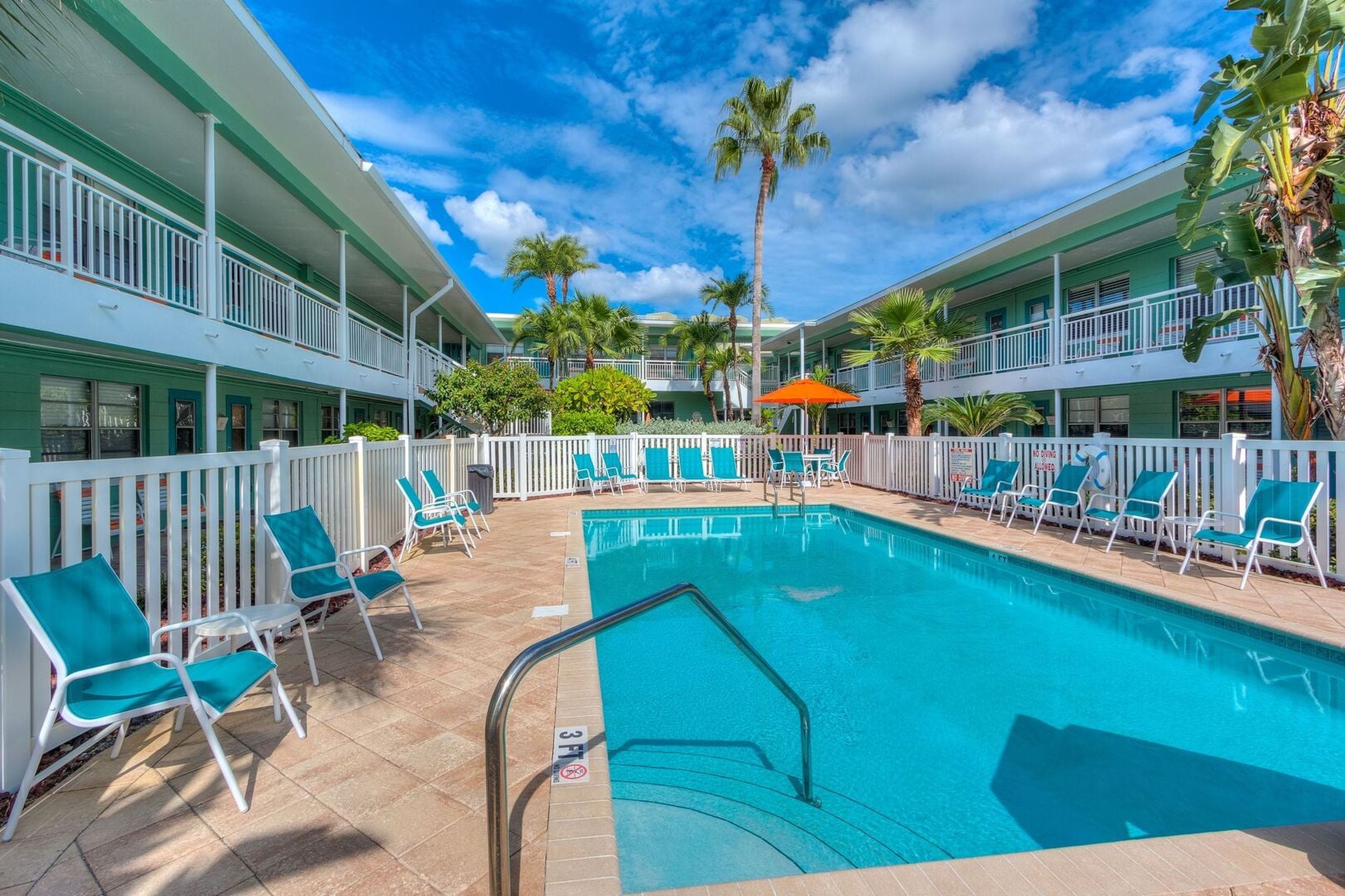 A hotel pool area with a clear blue pool, white railings, and multiple lounge chairs.