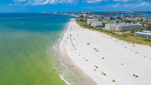 A beach with a long stretch of sand, a few umbrellas, and buildings in the background. - Tropic Terrace #56 | Pool View Studio | Resort Amenities (Treasure Island)