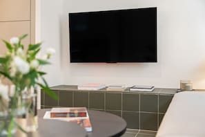 A modern living room with a flat-screen TV mounted on the wall, a round coffee table with a magazine, and a small plant. - Malasaña · Reformado · Gran Vía a 3 min a pie (Madrid)